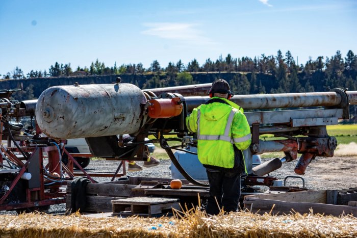A man operates a pumpkin canon at Smith Rock Ranch. He's wearing a bright yellow safety coat.