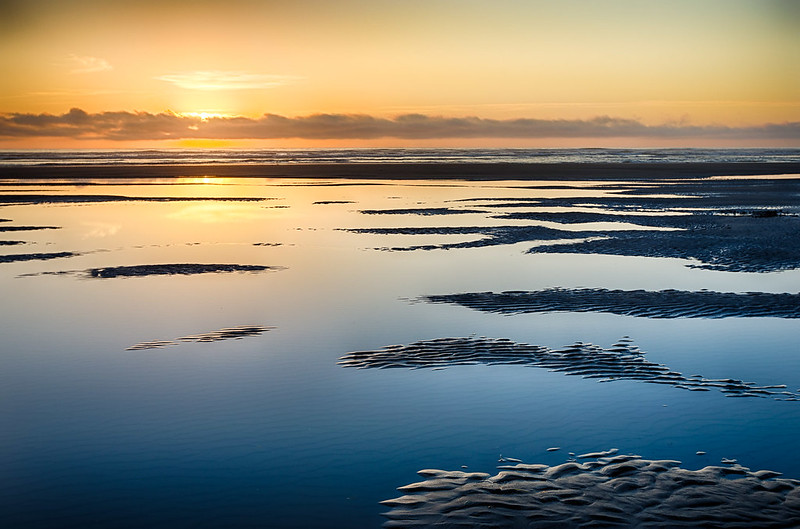 Seaside at sunset. It's a view of the beach covered in water with the sunset reflecting off of the still waters.