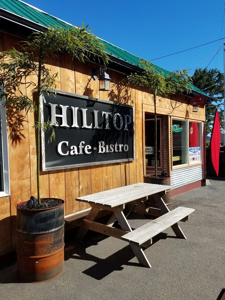 The outside of the Hilltop Cafe. A picnic table in front of the Hilltop Cafe sign between two potted trees.