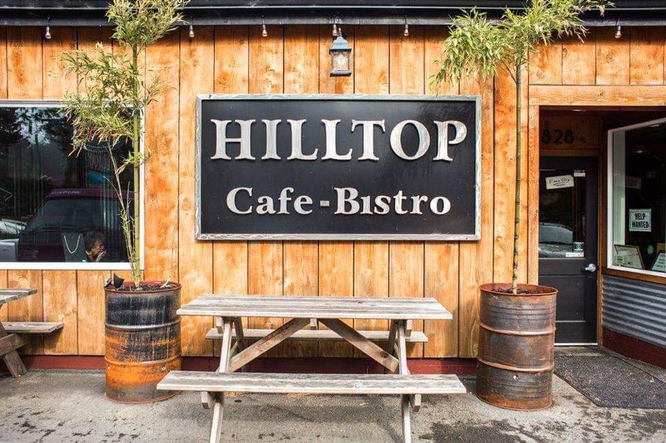 The outside of Hilltop Cafe Bistro. A warm wood wall with a picnic table and two trees in metal barrels.