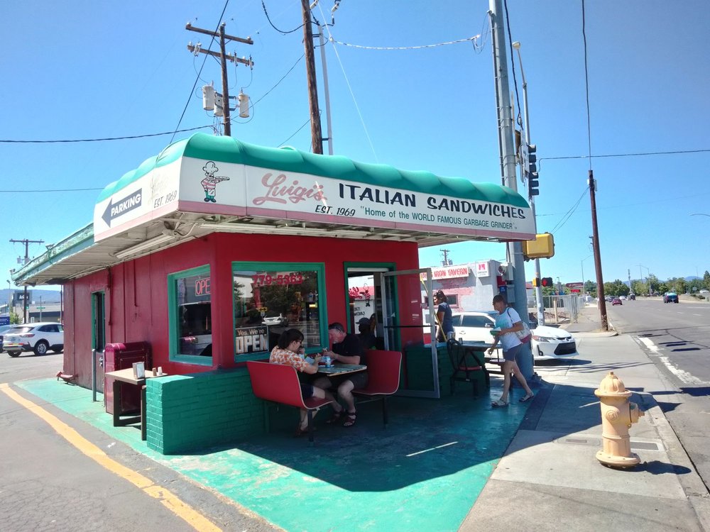 Lugi’s Italian Sandwiches. Photo via Yelp. The outside of Luigi's. It's a small red building with a green roof and green painted small outdoor seating area.