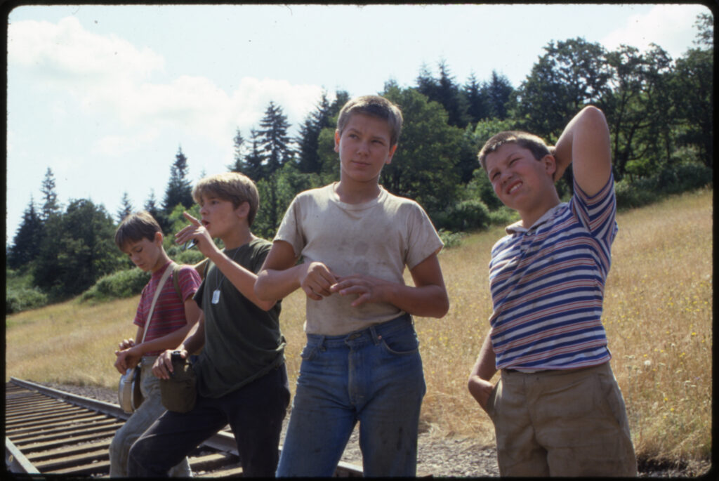 A photo of the four childhood actors in the movie Stand By Me standing next to each other in the sun and looking into the distance.