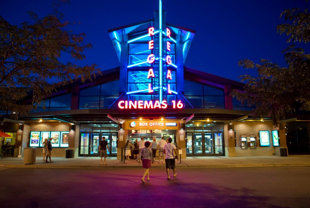 The outside of Regal Cinemas lit up at night with red and blue neon lights.
