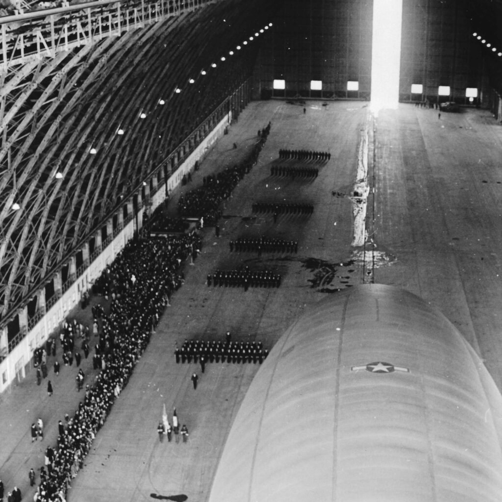 A black and white photo of inside Hangar B during an open house on July 4th, 1945. People line up and look at a massive blimp inside. tillamook air museum, planes, WWII, history, family things to do, oregon coast
