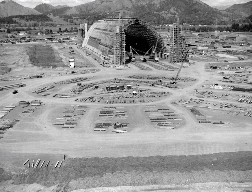 A black and white photo of massive Hangar B being constructed. There are organized piles of lumber all around the property waiting to be used in construction of the hangar. tillamook air museum, planes, WWII, history, family things to do, oregon coast