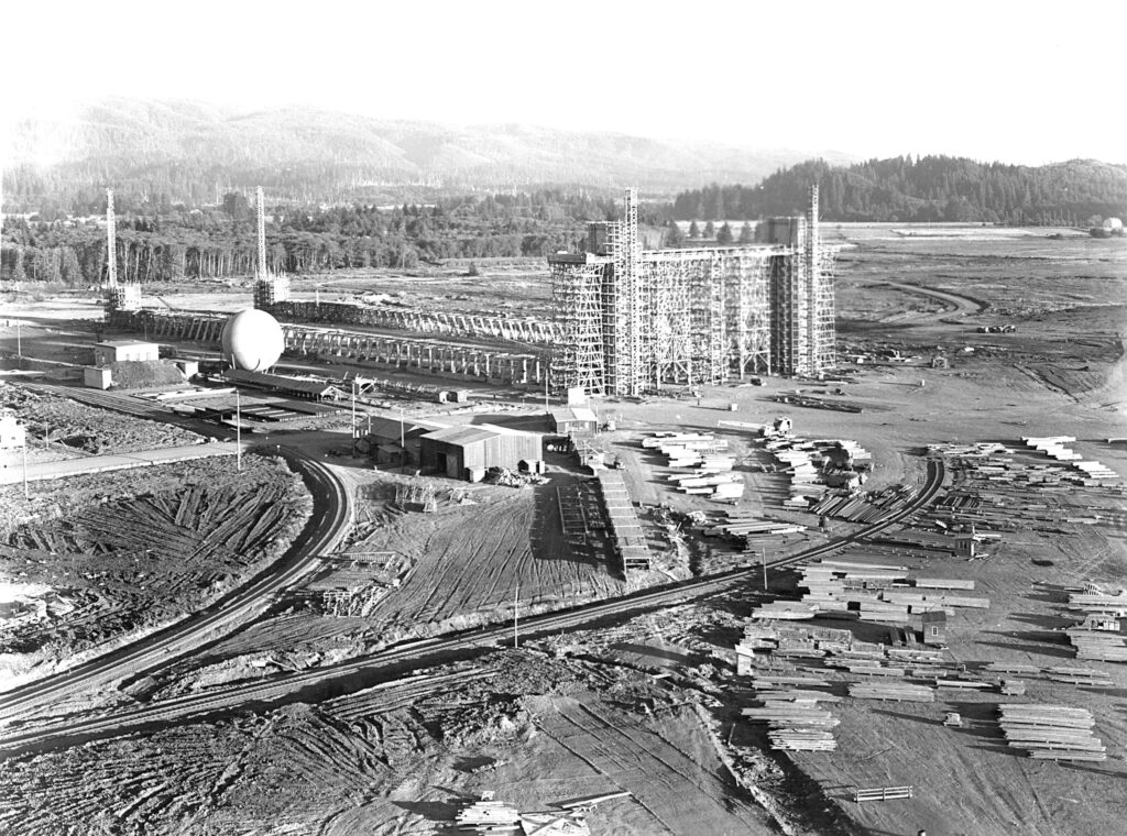 A black and white photo of massive Hangar B being constructed. The air hangar was just started and there are piles of lumber everywhere ready to be used in construction. tillamook air museum, planes, WWII, history, family things to do, oregon coast
