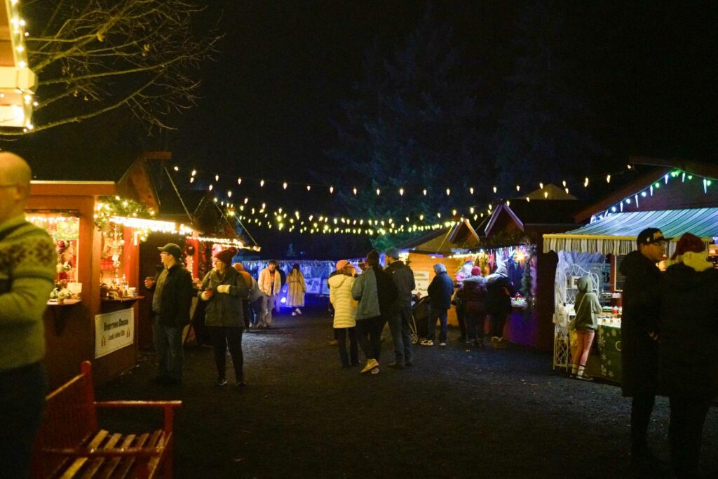 Food and craft booths at the Silverton Christmas Market. Warm white lights are strung overhead across the path.