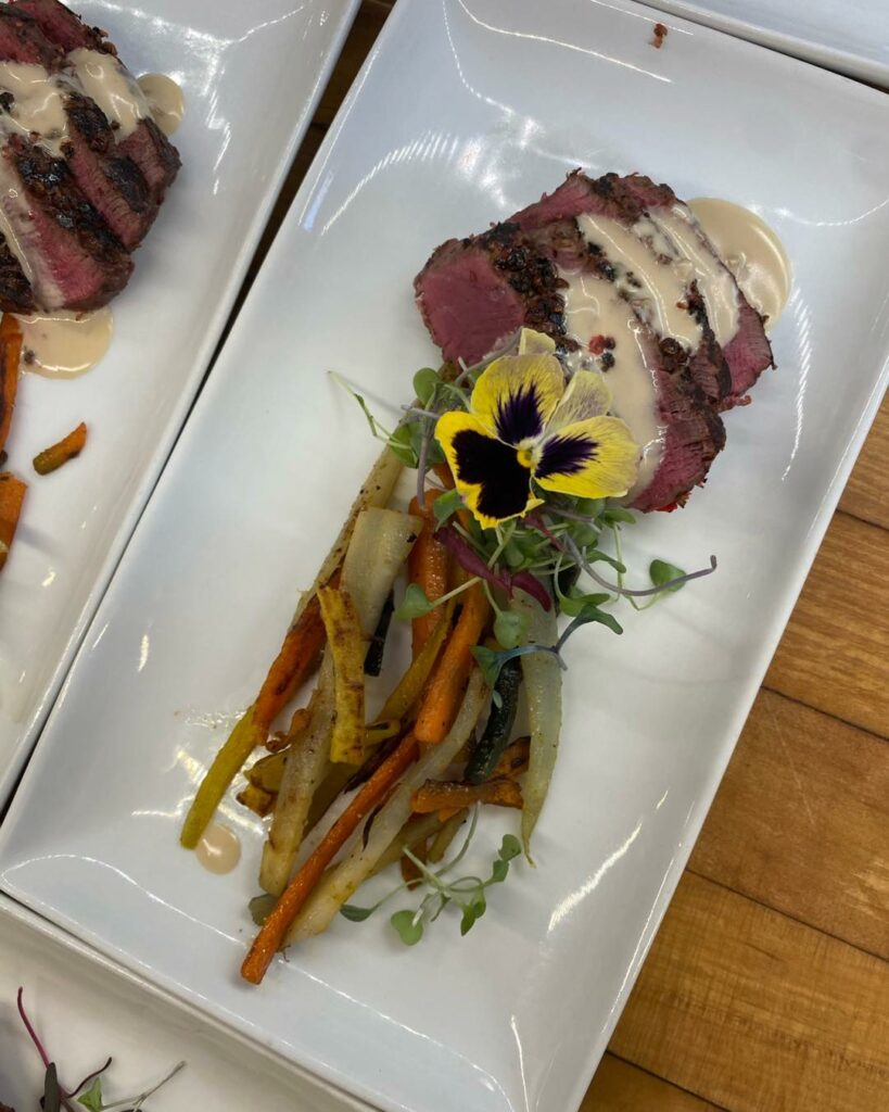 Cooked meat and vegetables arranged with a flower on a white plate.