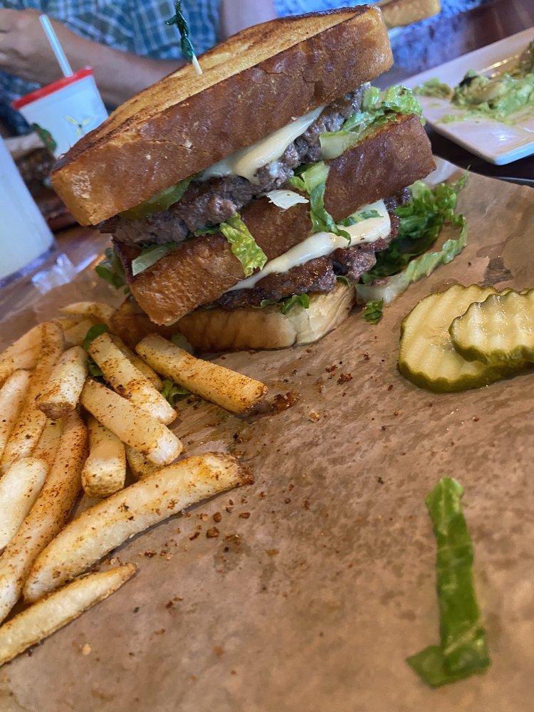 A burger with seasoned fries and two pickle slices on the side.