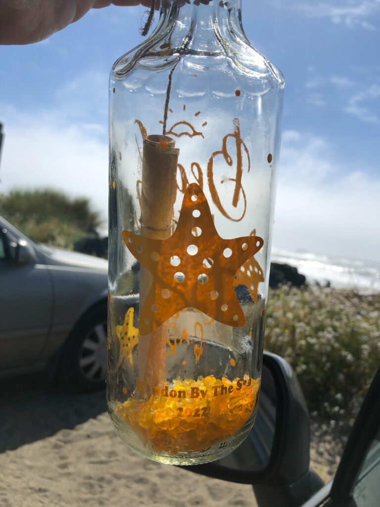 A clear bottle with a dark yellow painted starfish on it, and a rolled up scroll inside in Bandon, Oregon. It's part of the 'message in a bottle' event.