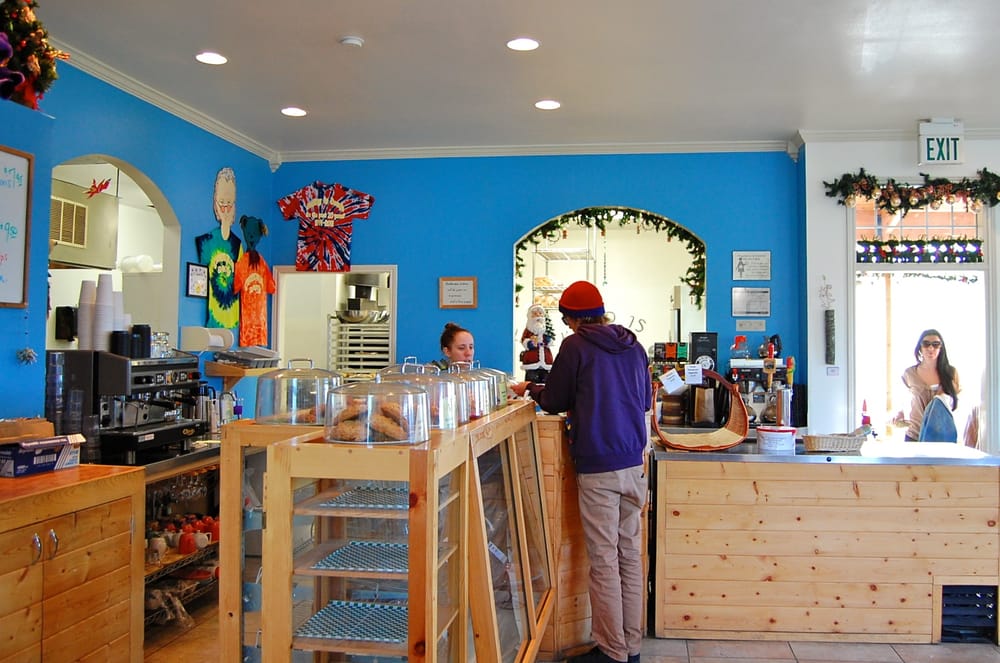 A woman serves a customer at a wooden counter. There's a bright blue wall behind her.