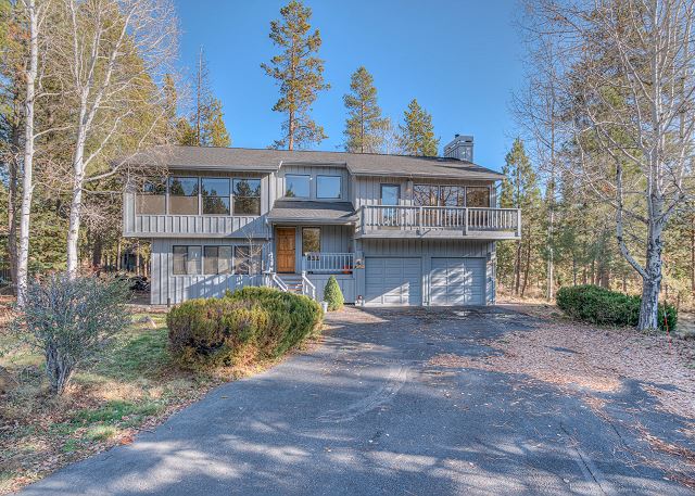 The outside of Belknap #4. It's a gray two story house with big windows and a second story porch over the double garage. There's a big driveway and trees in the background.