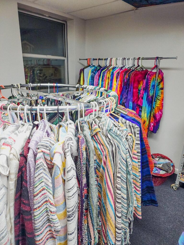 Colorful shirts on a circular rack, with tie dye hoodies in the background in vibrant colors at Love Works Hippie Store in Lincoln City, Oregon.
