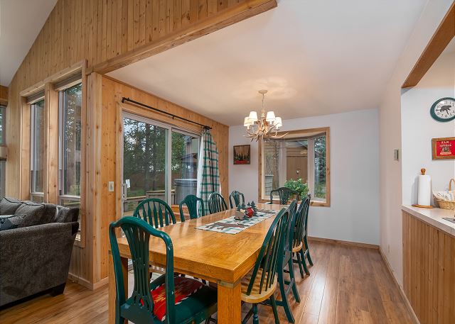 The inside of Duckpond #2. There's a large wooden dining table with ten green wooden chairs, and the interior of the house is done in light colored wood, and shades of white and green.