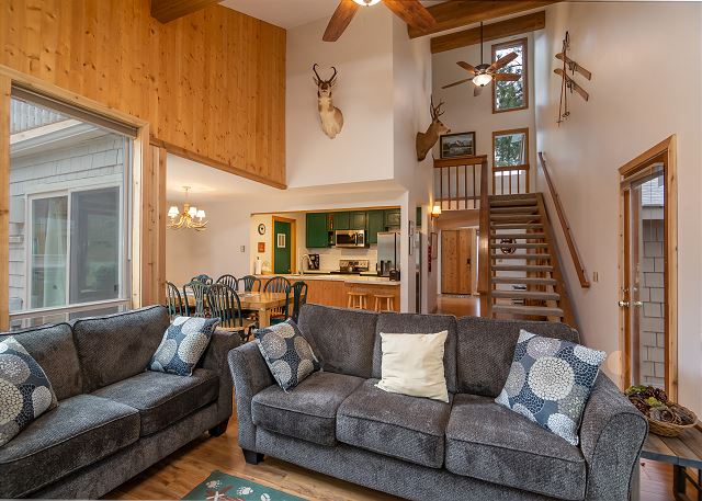 The inside of Duckpond #2. There are comfortable lookin gray fabric couches in the living room, and the interior of the house is done in light colored wood, and shades of white and green.