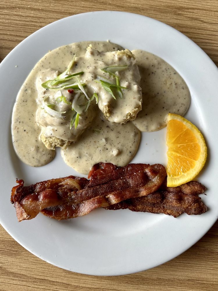 A white plate with eggs, half an orange slice, and biscuits and gravy.