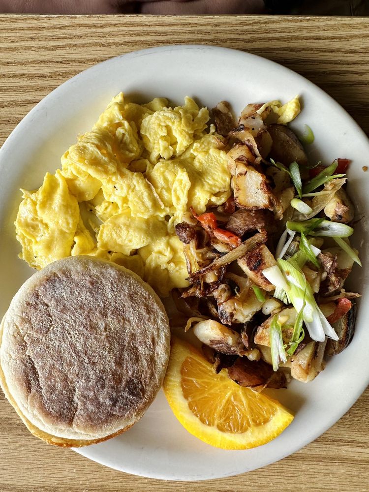 Scrambled eggs, potatoes and an English muffin plated in an aesthetically pleasing way.