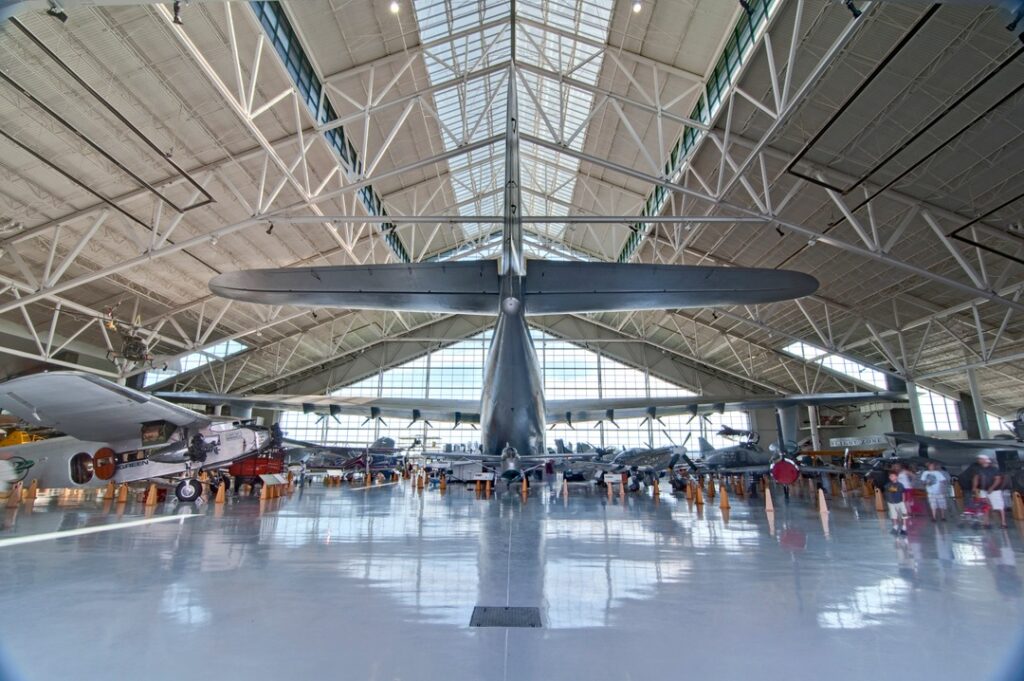 The Spruce Goose inside the Evergreen Aviation And Space Museum. It takes up a huge amount of space in the main museum area. It sits in front of large windows, casting the massive plane in daylight.