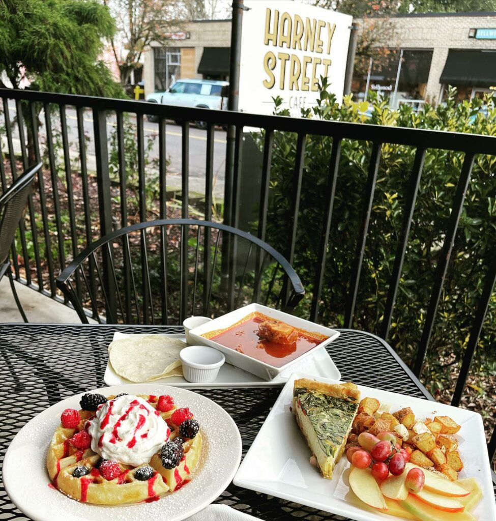 Several plates of delicious looking food on a black metal table with the Harney Street Cafe sign in the background.