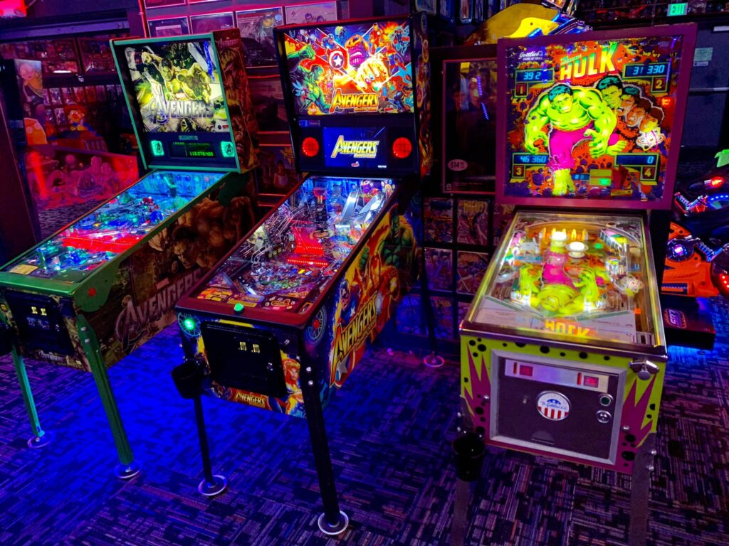 Several brightly lit Avengers themed pinball machines inside Next Level Pinball. The room is kind of dark, so the pinball machines are all lit up brightly. Looks like lots of fun!