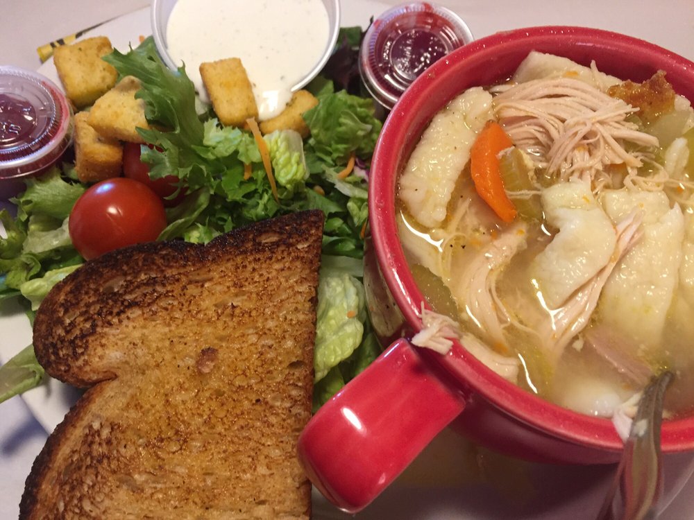 Homemade chicken noodle soup in a big red mug. Toast and a salad are next to it on a plate.