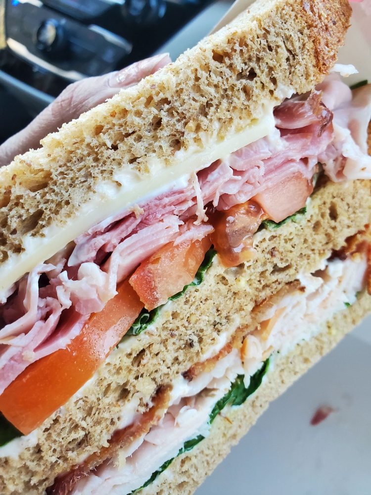 A sandwich stacked with two kinds of meat, tomato, cheese, and a thin layer of greens on bread.
