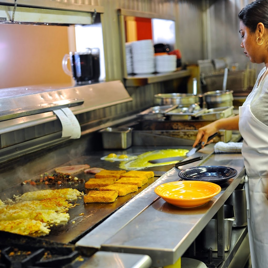 A woman makes breakfast foods in the kitchen. There are hash browns, French toast, and eggs being made.