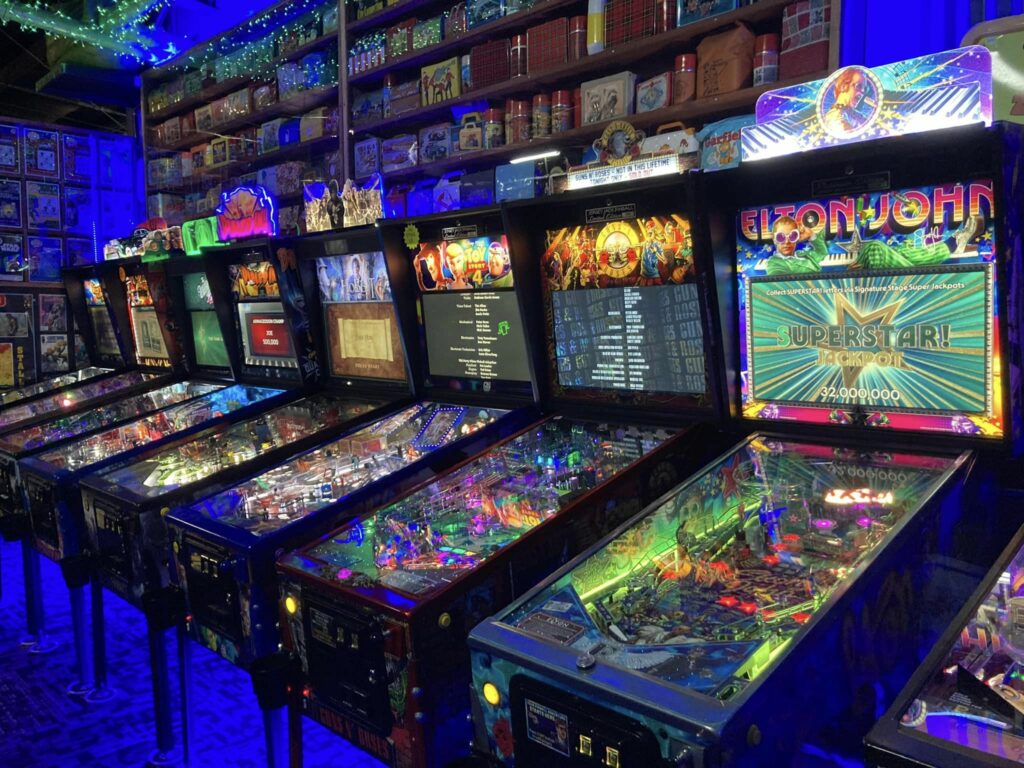 Several brightly lit pinball machines inside Next Level Pinball. The room is kind of dark, so the pinball machines are all lit up brightly. Looks like lots of fun!