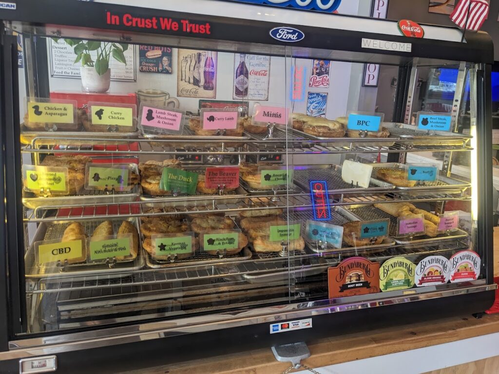 A glass display case full of a variety of fresh meat pies.