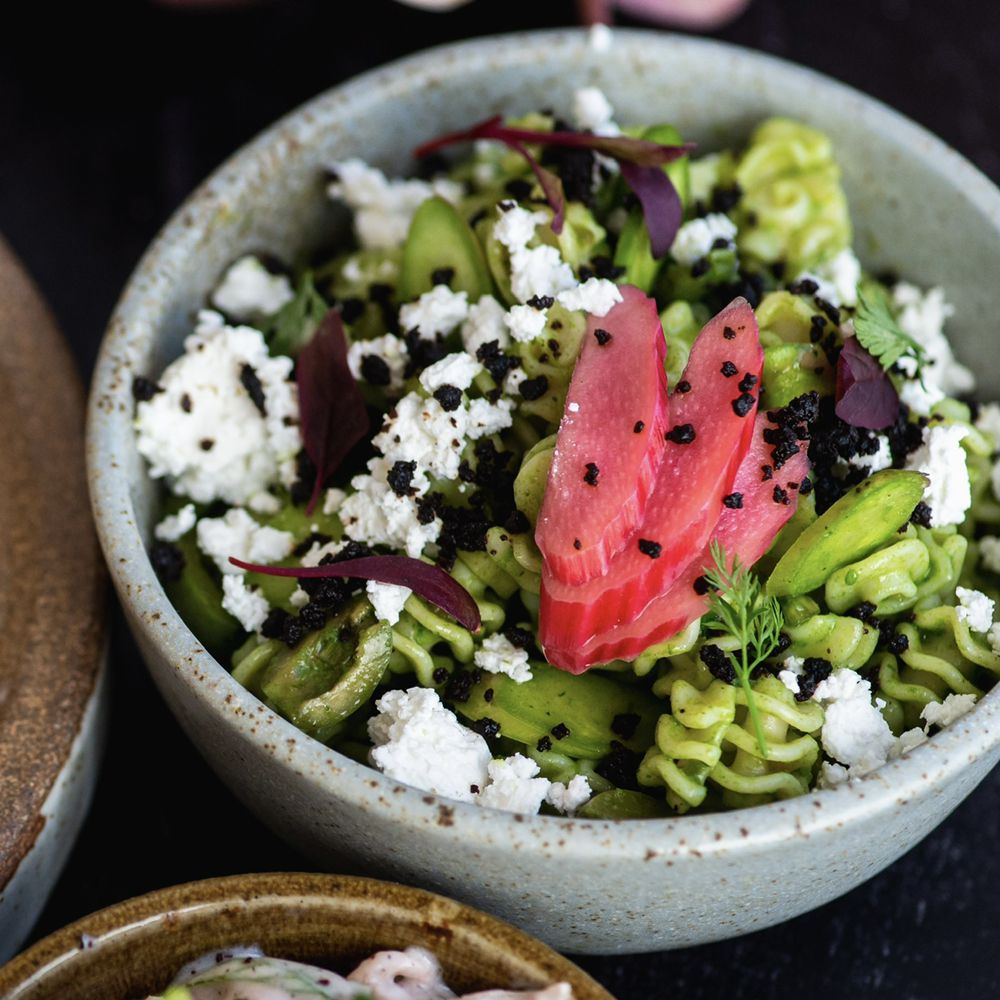 A colorful bowl of green pasta with colorful toppings.