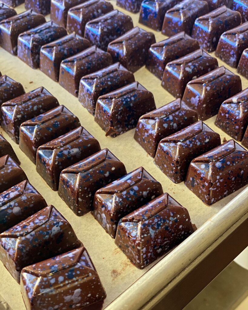 Shiny fine chocolates. The chocolate shell is speckled with blue and white and looks a little like a starry galaxy.