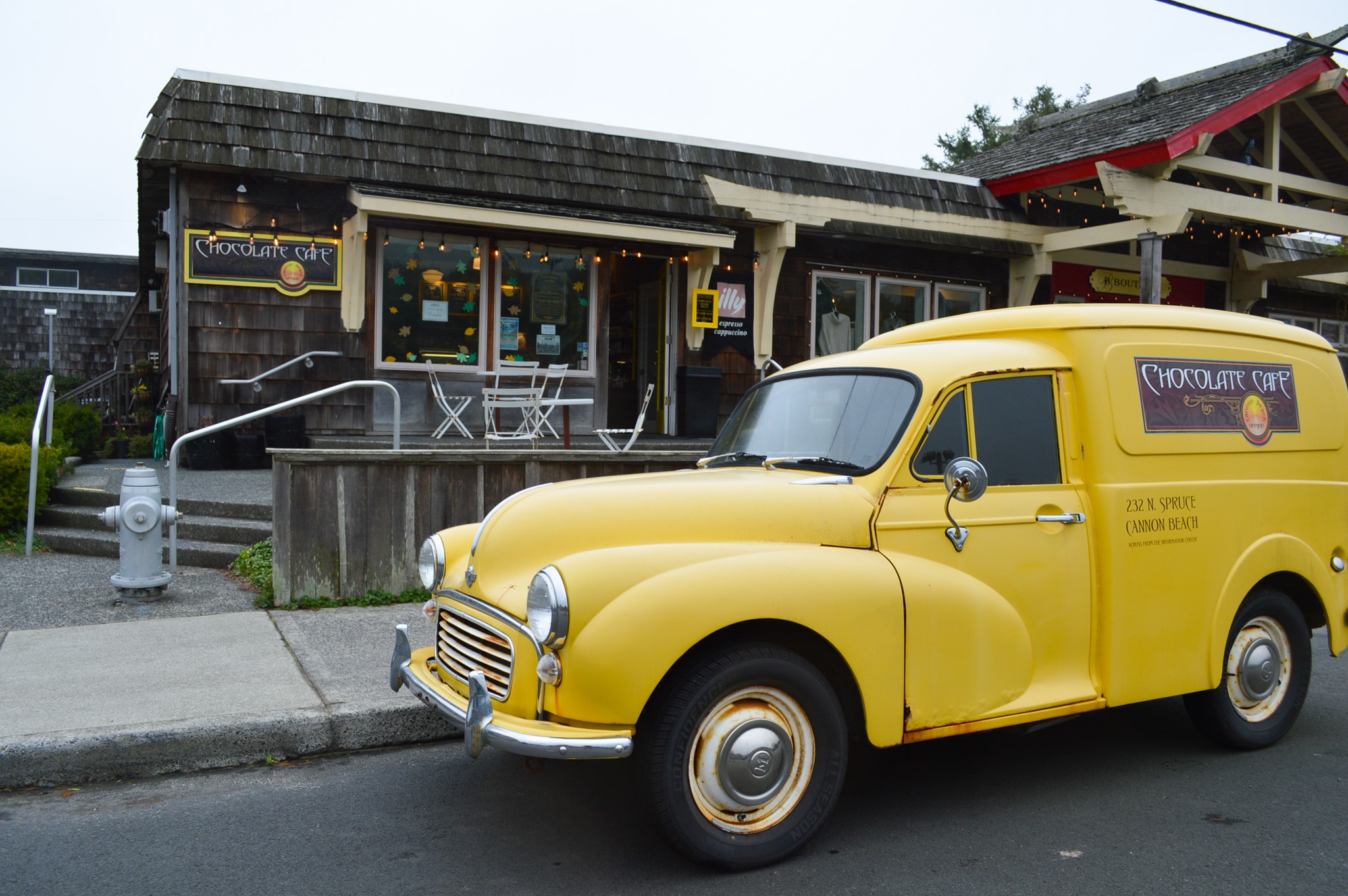 Photo via the Cannon Beach Chocolate Cafe Facebook The outside of the Cannon Beach Café. There's an old vintage yellow delivery truck parked out front.