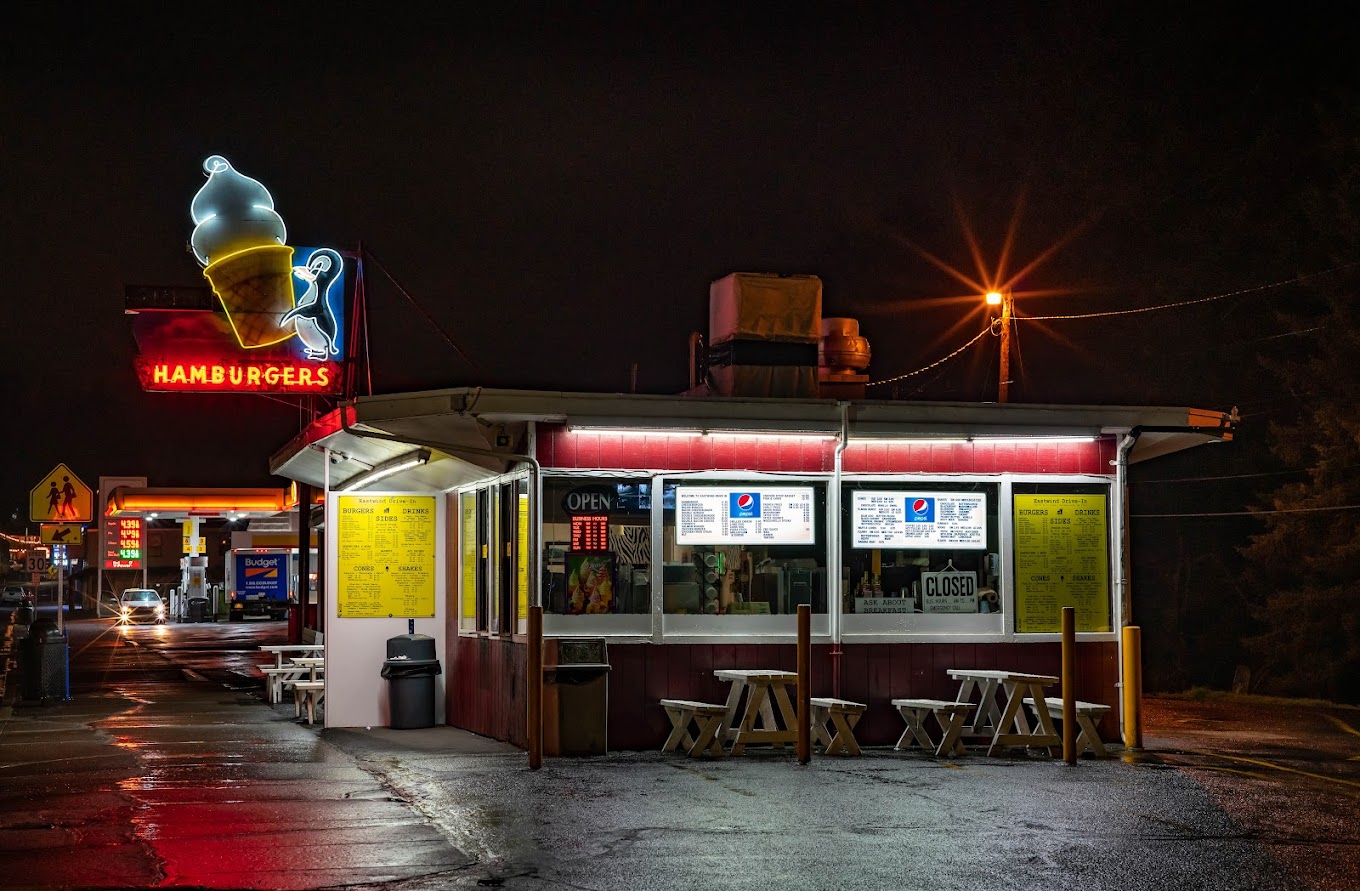 Photo by Phillip McMillen via Google Local. The outside of Eastwind Drive-In at night. There's a neon sign with an ice cream cone lit up with red lettering.