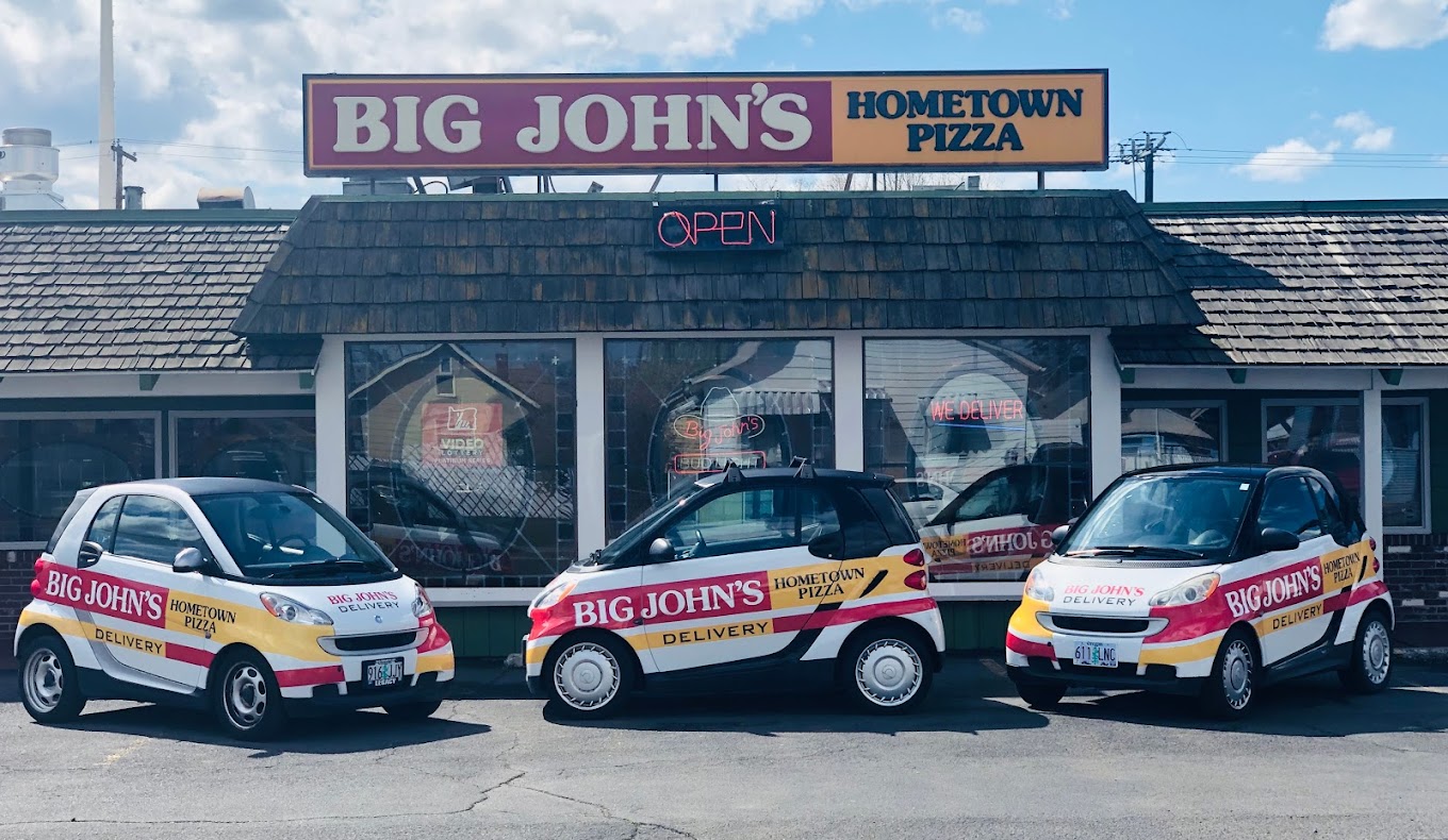 Photo by Big John’s Hometown Pizza via Google Local. The outside of Big John's Pizza in Pendleton, Oregon. In the photo there are several little white delivery cars for Big John's parked out front.