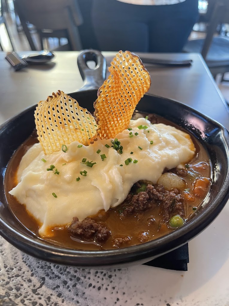 A delicious looking meat dish covered in fluffy white mashed potatoes in a black bowl. It looks hearty and so delicious!