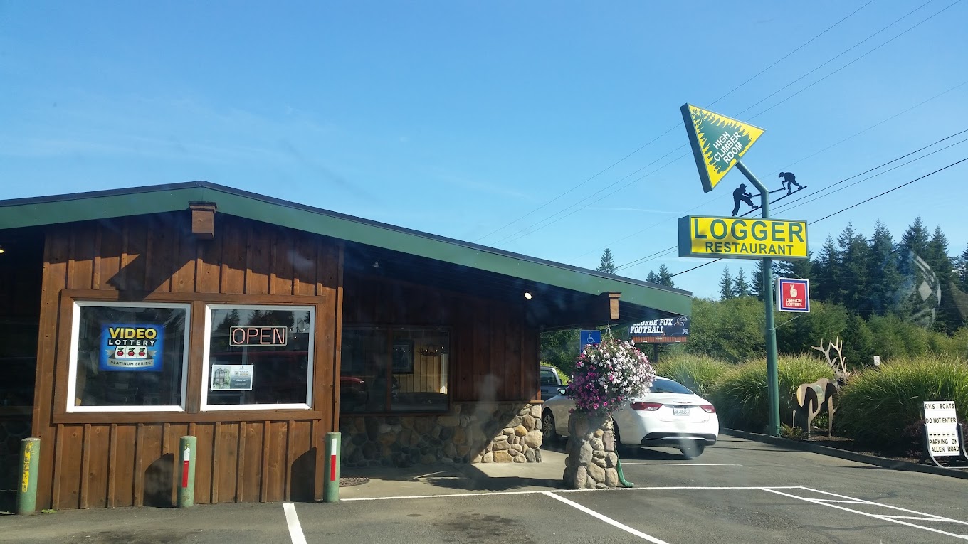 Photo by Erlyn Sweitzer via Google Local. The outside of The Logger Restaurant in Knappa near Astoria, Oregon. The outside is a dark wood with green trim. There's a bright yellow and green sign with a tree and an arrow pointing into the air.