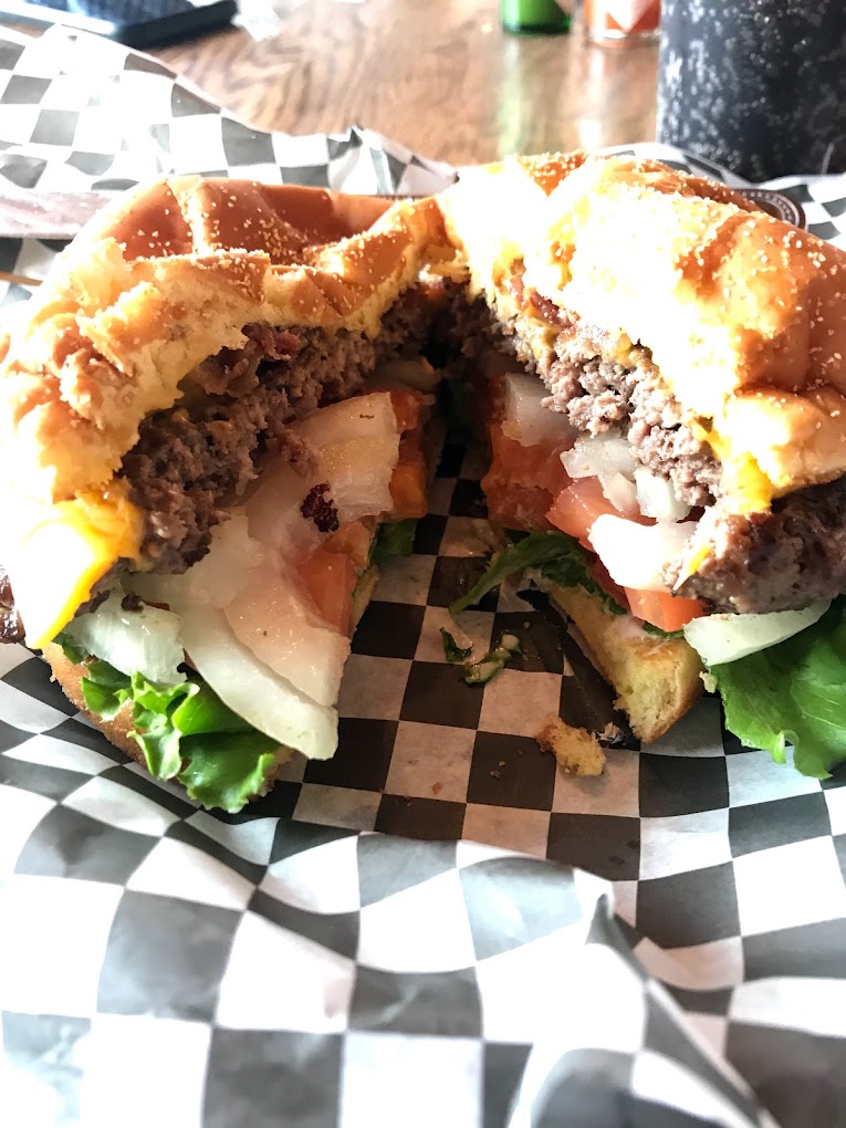 A burger cut in half on a black and white checkered paper wrapper. It has onions, lettuce and tomato on it.