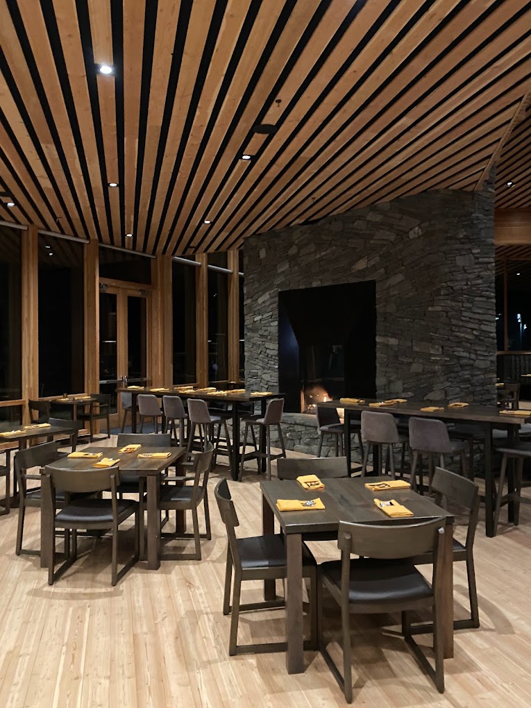 The interior of the Lodge Restaurant. It features a stone fireplace, soft wood tones, modern furniture, and modern Pacific Northwest architecture.