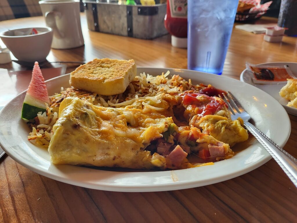 A plate full of a large portion of hash browns, an omelet and a piece of toast.