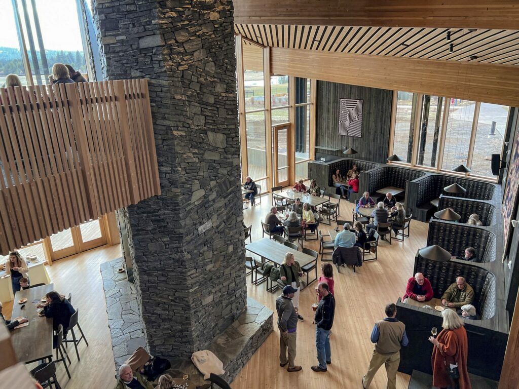 The interior of the Lodge Restaurant. It features a two story tall stone fireplace, soft wood tones, modern furniture, and modern Pacific Northwest architecture.
