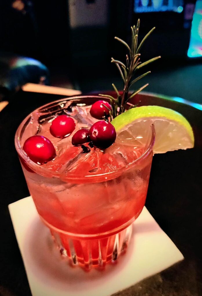 A red drink with red berries and a lime wedge.