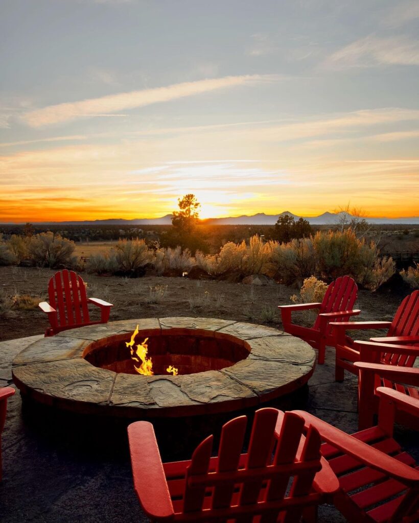 The firepit at Brasada Ranch at sunset. It's surrounded by flagstones and several red Adirondak style chairs.