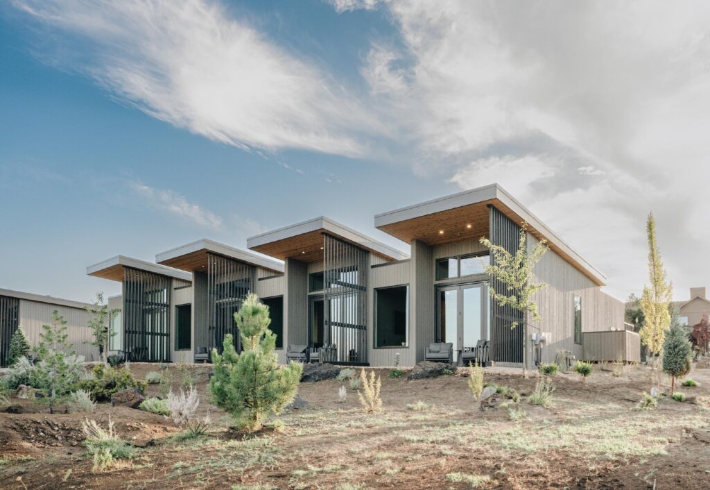 The exterior view of the bungalows. They are gray, modern, have big windows, and one sloped roof on each.