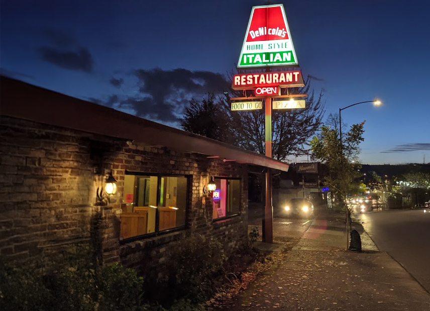 Photo by Joaquin Diaz via Google Local. The outside of DeNicola's restaurant at night. A large red, white, and green sign lights up the area proclaiming: 'DeNicola's Home Style Italian Restaurant, Open, Food To Go, Pizza.'