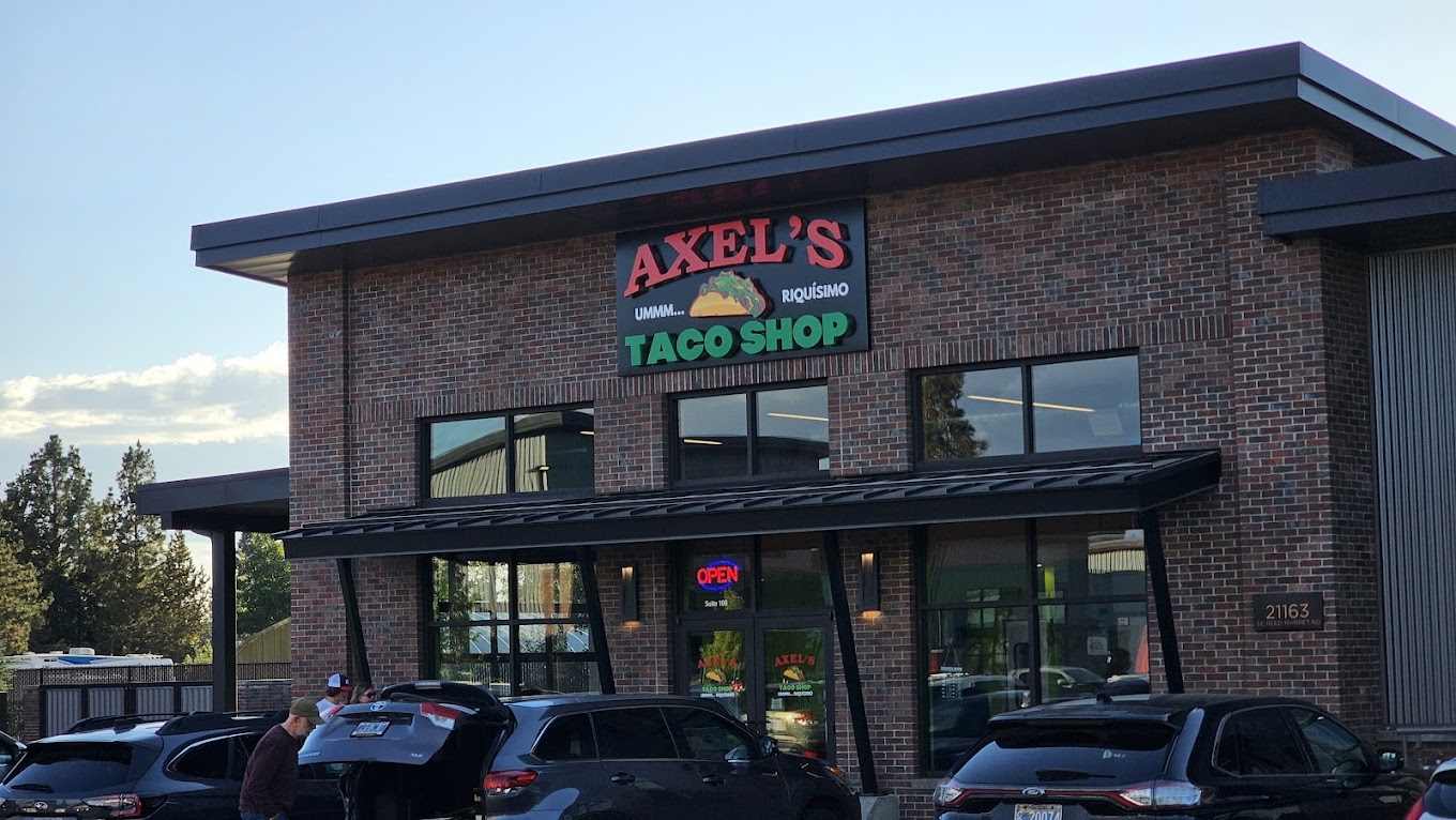 Photo by Axel’s Taco Shop via Google Local. The outside of Axel's Taco Shop. It's a brick building with a large red and green sign on the front.