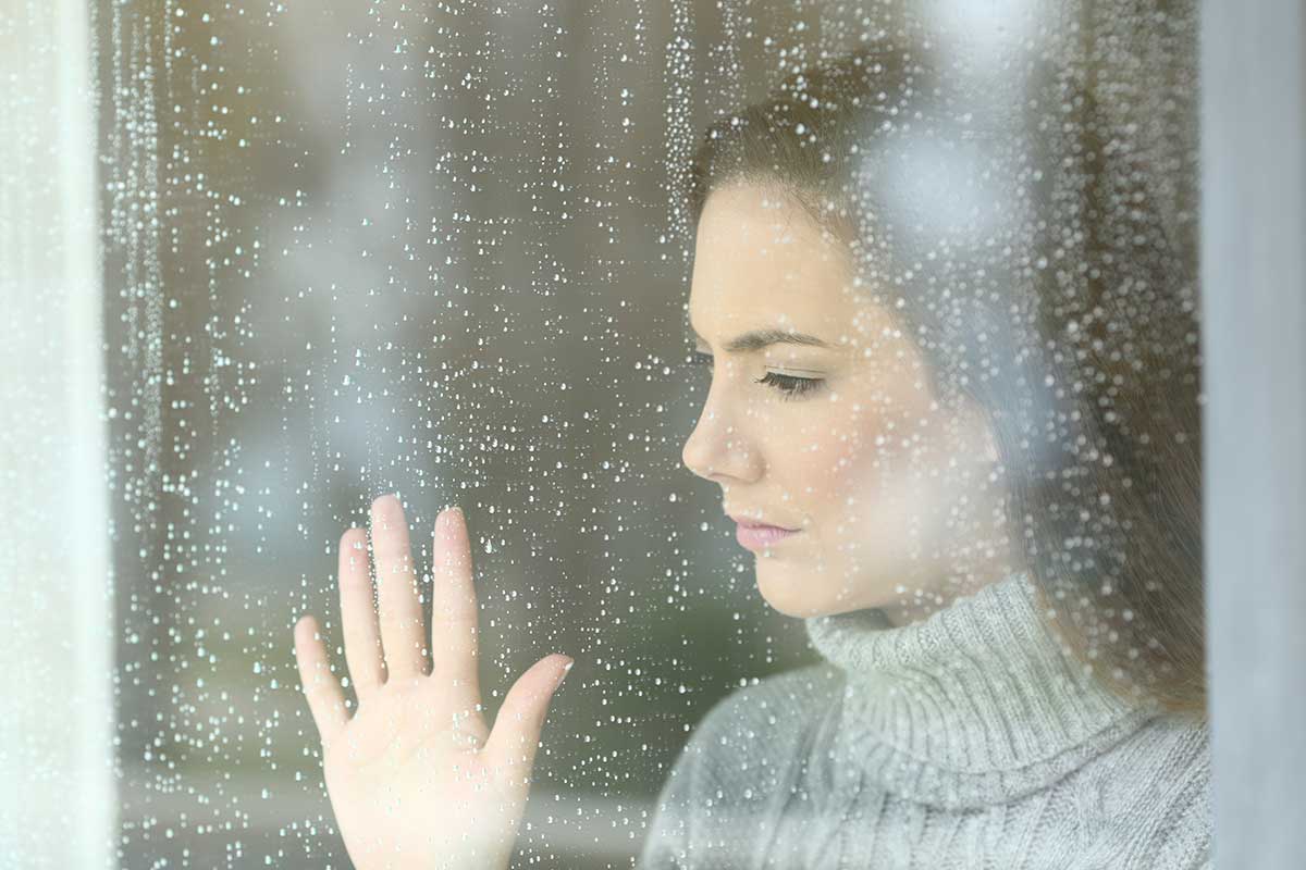 shutterstock_789160546 poor woman looking outside at the rain