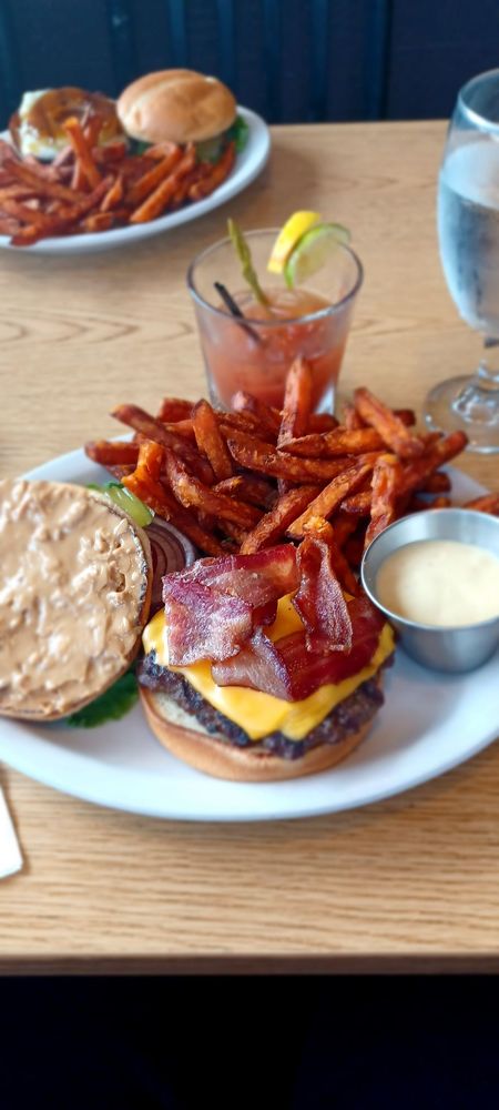 A burger with bacon, cheese and sauce on a plate with sweet potato fries.