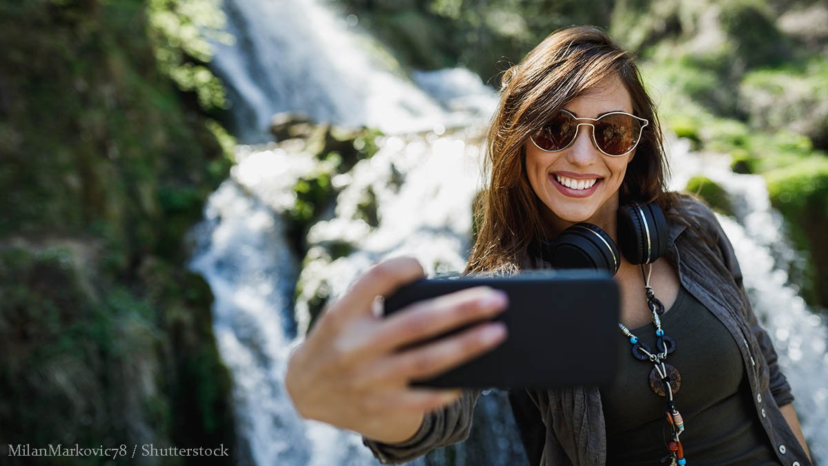 A,Smiling,Young,Woman,Making,Selfie,With,Her,Smartphone,While woman hiking waterfall