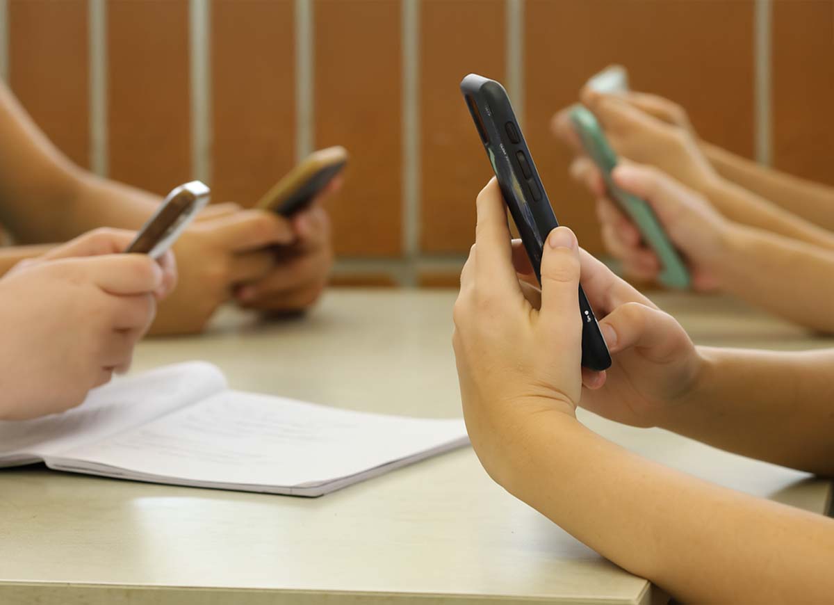 Governor Kotek Bans Cell Phones In Oregon Schools 2025 Students sit at a desk looking at their cell phones.