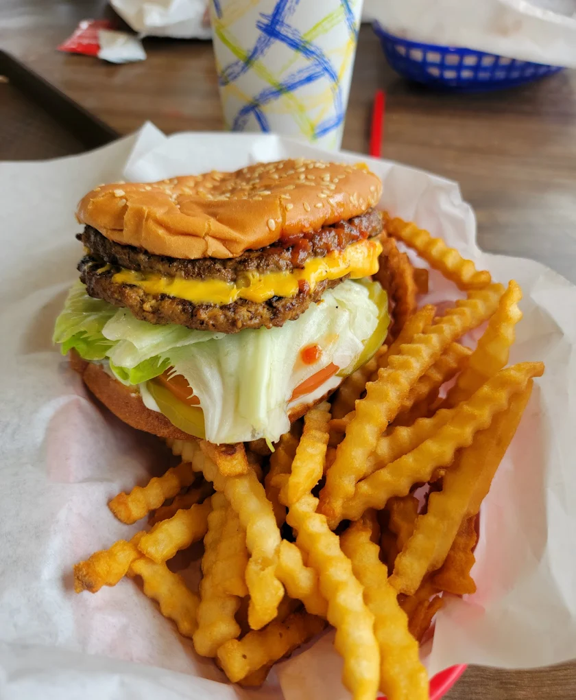 A thick juicy burger with two patties, cheese, lettuce and bacon, and a basket of fries.